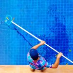 man scooping dead leaves out of pool